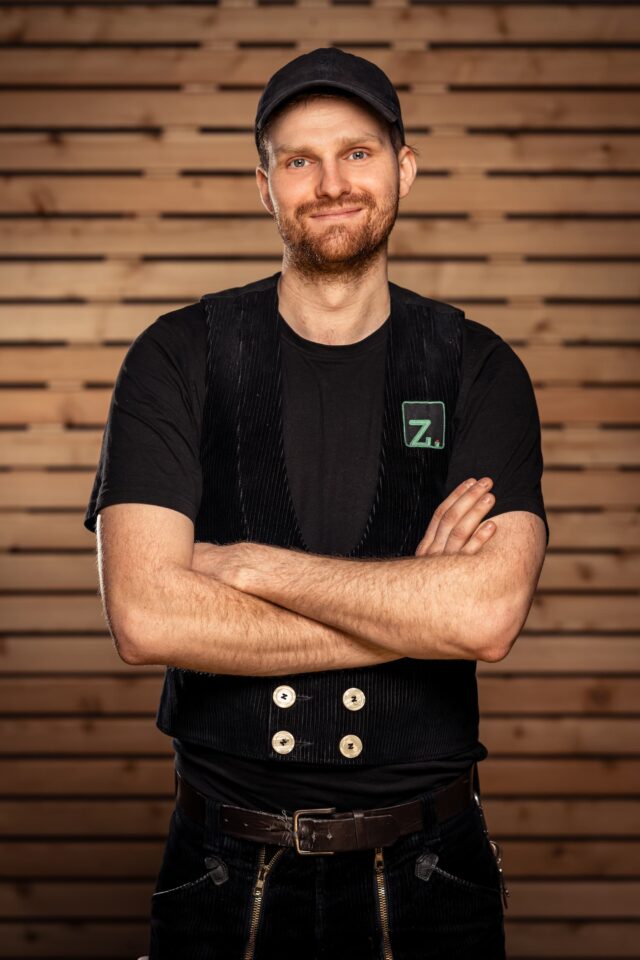 Mann mit schwarzem T-Shirt und Cap vor Holzpaneelen, Zimmerei Freiburg.